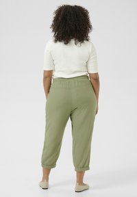 Green elastic-waist pants with tapered cuffs, made from a soft material, paired with a fitted beige top featuring short sleeves.