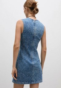 Denim obleka v modrem pranju s prilagojeno silhueto, brezrokavnim dizajnom in razporkom z zadrgo na hrbtni strani. Ima subtilen teksturni vzorec in šivane poudarke.