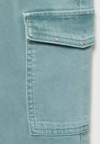 Svijetloplav fabric s bližim pogledom na džep koji ima srebrne dugme za kopčanje i vidljive detalje šivanja.