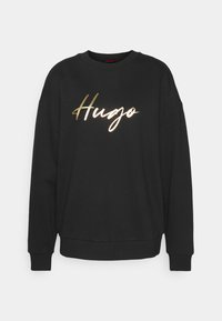 Zwarte trui van zachte stof, met een ronde hals, verlaagde schouders en een goudkleurig scriptlogo met de tekst "Hugo" op de voorkant.