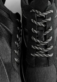 Sneaker nere caratterizzate da una combinazione di suede e pelliccia testurizzata, con lacci bianchi e neri in contrasto e dettagli di cucitura delicati.