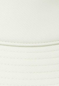 Witte honkbalpet van een gestructureerde, geribbelde stof. Heeft gestikte details langs de klep en een gladde kroon.