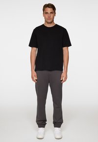 T-paita, jossa on mustat lyhyet hihat, yhdistetty tummanharmaisiin verkkareihin, joissa on ribbireunat ja joustava vyötärö. Mallilla on valkoiset lenkkarit.