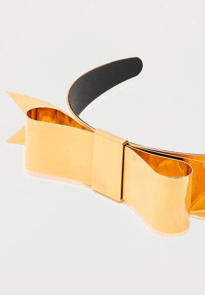 Χρυσή μεταλλική κορδέλα με λαμπερή λεπτομέρεια σε σχήμα φιόγκου και εσωτερικό μαύρο επενδυμένο σε λευκό φόντο.