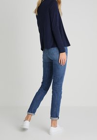 Marinblå långärmad topp tillsammans med ljusblå jeans uppvikta i ärmarna, bärs med vita sneakers. Mjuk textur med avslappnad passform.