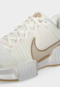 Λευκό και μπεζ αθλητικό παπούτσι Nike με υφασμένο επάνω μέρος, κλείσιμο με κορδόνια και χοντρή καουτσούκ σόλα με διάφορα σχέδια.