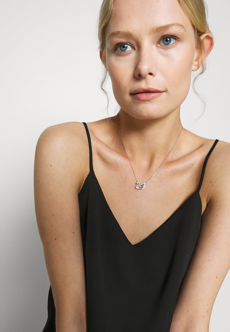 Black camisole top with thin straps; model wearing a silver necklace featuring a swan design adorned with rhinestones.