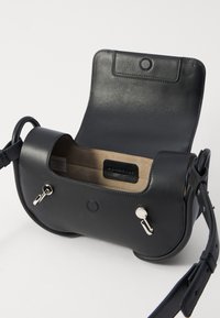 Borsa a tracolla in pelle nera con esterno liscio, forma arrotondata e chiusura a scatto. L'interno presenta una fodera in suede beige e dettagli di branding.