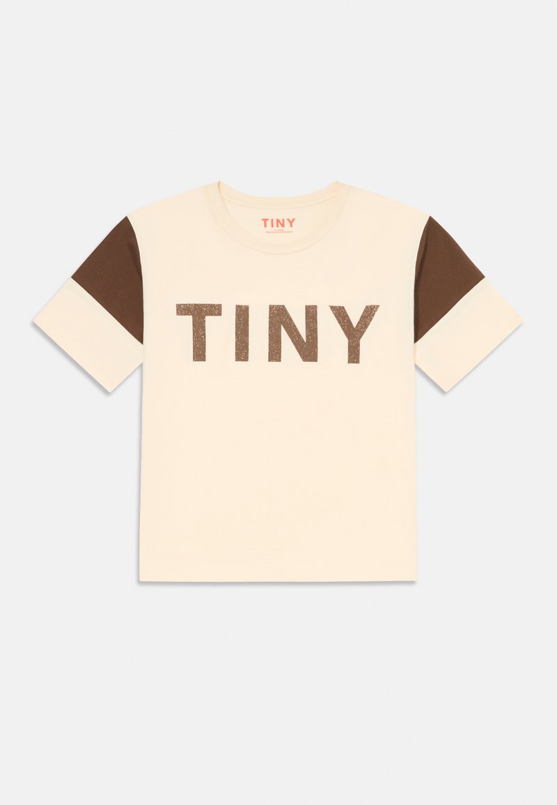 T-shirt crème avec des manches courtes marron, arborant le grand texte en paillettes marron "TINY" sur le devant. Design classique à col rond.