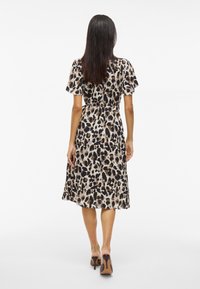 Vestido con estampado de leopardo que presenta mangas cortas, cintura con cinturón y falda fluida. Hecho de tela ligera con una textura suave.