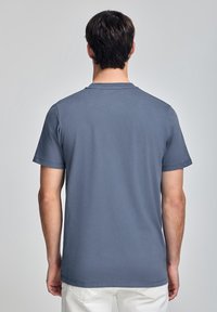 Grå t-shirt med korta ärmar och rund halsringning, tillverkad av mjukt bomullstyg. Har en rak fåll och minimal detaljering.