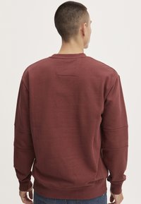 Bordo dukserica s okruglim izrezom, rebrastim rukavima i donjim rubom. Sadrži teksturiranu aplikaciju na leđima. Izrađena od mekanog, rastezljivog materijala.