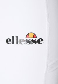 Biały materiał z czarnym logo "ellesse" oraz kolorowym półkolem nad nim. Gładka tekstura z widocznymi detalami szwów.