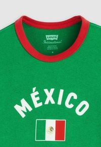 Πράσινο T-shirt με κόκκινο γιακά, λευκό κείμενο "MÉXICO" και τη σημαία του Μεξικού στο κέντρο κάτω, μέγεθος medium, κατασκευασμένο από τη Levi's International στο Πακιστάν.