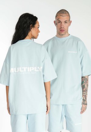 Las camisetas de algodón de gran tamaño en azul claro presentan el texto "MULTIPLY" en blanco en la parte de atrás, combinadas con pantalones cortos a juego para un look coordinado.