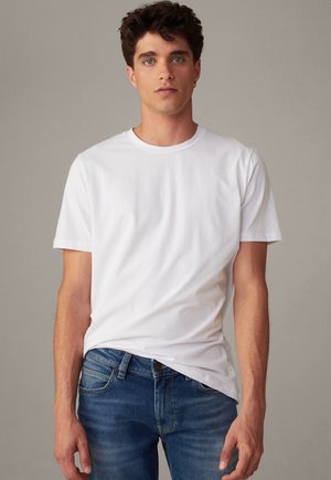 Witte katoenen t-shirt met korte mouwen en een ronde halslijn, gedragen met blauwe denim jeans. Gladde textuur, minimaal ontwerp, geen patronen.