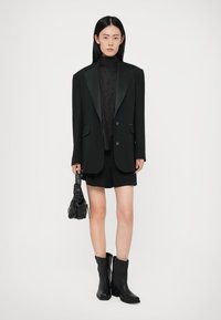 Black blazer with satin lapels, fitted turtleneck, tailored shorts, and black ankle boots. Includes a small black textured handbag.