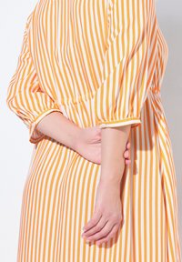 Abito a righe arancione e bianco, con maniche a tre quarti, un fit morbido e una texture di tessuto morbido. Decorato con dettagli arricciati.