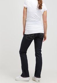 Mörkblå denimjeans med utsvängd passform, med sydda bakfickor och en slät yta, ihop med en åtsittande vit T-shirt och vita sneakers.