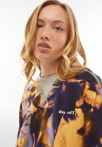 Colorful sweatshirt featuring an abstract floral pattern in orange, blue, and purple. Light gray neckline with "day off" printed in white.
