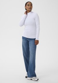 Bluză albă cu guler înalt, cu mânecă lungă și textură ribbed, asortată cu blugi largi albaștri și teniși sport cu un model din plasă.