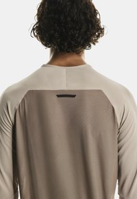 Langarm-Sportshirt in hellem Beige mit einer strukturierten Rückenpartie und einem schwarzen Akzent. Es hat einen Rundhalsausschnitt und Raglanärmel.