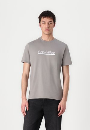 Grijze katoenen t-shirt met ronde hals en korte mouwen, met een witte "Calvin Klein" logo over de borst. Glad textuur, reguliere pasvorm.