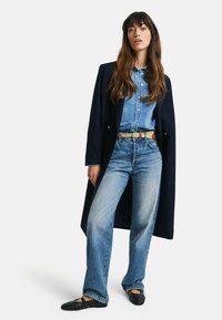 Mørkeblå lang frakk, lyseblå denimskjorte, lyseblå jeans og svarte vevde hæler. Har et mønstret belte, avslappet passform og knappe Detaljer.