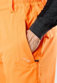 Orange STX™ 8000 byxor har en texturerad fabrik, en elastisk midja och en sidoficka med en svart dragkedja.