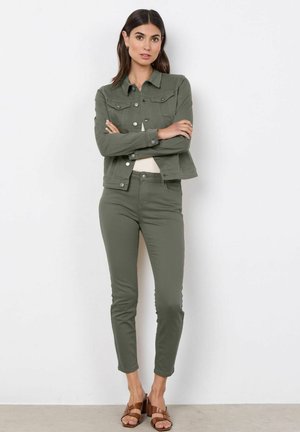 Olive green denim jacket with button closures and a structured collar, paired with matching fitted olive green pants and brown heeled sandals.
