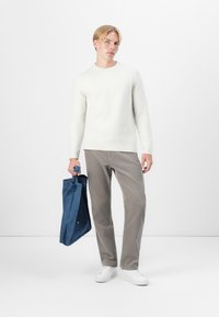 Bel bela teksturirana pulover, sivi kordurovski hlače in modra denim torba; model stoji v belih supergah na enobarvni podlagi.