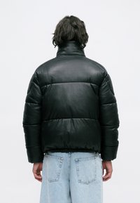 Jachetă puffer din piele neagră, cu guler înalt, tiv elastic și secțiuni quilted orizontale, asortată cu blugi din denim albastru deschis.