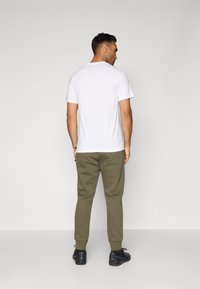 T-shirt branca de algodão com mangas curtas, combinada com calças de treino verde-oliva feitas de tecido macio e sapatos de desporto pretos. Vista traseira.