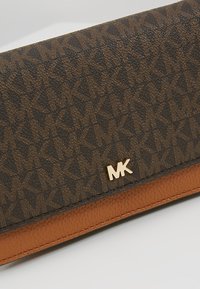 Portefeuille texturé marron et noir avec motif répétitif "MK", garniture en cuir fauve et logo "MK" doré sur le rabat avant.