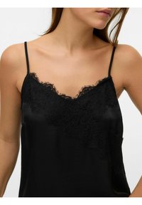 Svart sateng-kamisole med tynne stropper, med blonder over halsutskjæringen og en glatt, skinnende tekstur.