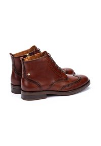 Bottines en cuir marron avec des détails de brogue décoratifs, fermeture à lacets et semelle plate. Texture lisse et design de bout légèrement pointu.