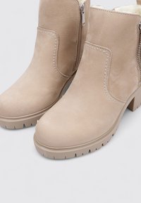 Botas de tobillo beige con acabado de ante texturizado, cierre de cremallera, tacón grueso y suela robusta para mayor agarre y durabilidad.