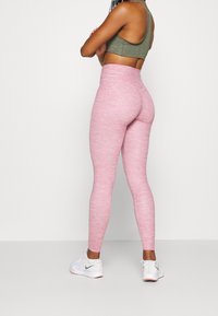 Leggings rosa a vita alta realizzati in un tessuto testurizzato, abbinati a un reggiseno sportivo verde. Scarpe da ginnastica bianche con accenti grigi.