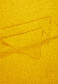 Tissu texturé jaune à finition douce, comportant des formes triangulaires superposées, créant un motif visuel distinct.