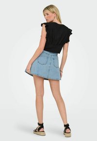 Schwarzes kurzärmeliges Oberteil mit Rüschendetails, kombiniert mit einem Jeans-A-Linien-Rock. Das Outfit hat eine figurbetonte Taille und einen lässigen Look.