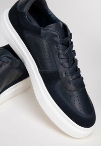 Granatowe skórzane sneakersy z perforowanym wzorem, zamszowymi akcentami, okrągłym noskiem i białą gumową podeszwą. Widoczne sznurowadła i podszewka.
