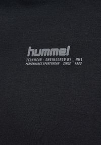 Svart textil med tryckt vitt varumärke. Innehåller "hummel"-logotypen och "TECHWEAR - ENGINEERED BY _HML PERFORMANCE SPORTSWEAR SINCE 1923."