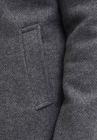 Hallikassooniline villane kangas, millel on kalasaba muster ja vasakul küljel ristkülikukujuline tasku. Pehme ja soe välimus.