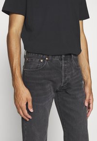 Schwarze, enganliegende Jeans aus Denim mit Kupfer Hardware, Fünf-Taschen-Design und subtiler Abnutzung im Stoff.