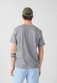 Grijs katoenen T-shirt met korte mouwen, losse pasvorm, ronde hals en een gladde textuur. Gecombineerd met lichtblauwe spijkerbroek.