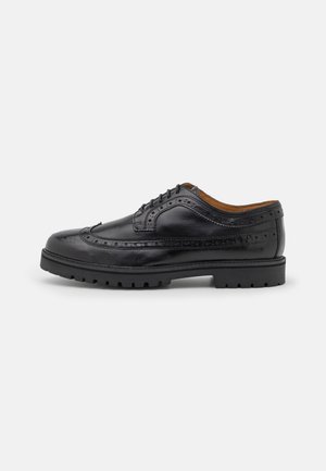 Chaussure habillée brogue en cuir noir avec perforations décoratives, fermeture à lacets et semelle en caoutchouc épaisse, vue de côté droit sur fond blanc.