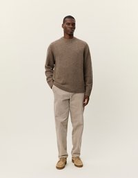 Pull en tricot marron avec un col rond, pantalon en velours côtelé beige et chaussures brun clair. Design simple, texture douce, sans motifs ni accents.