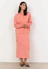 Koraalroze hoodie met een knopenlijst en dubbele borstzakken, gecombineerd met een bijpassende maxi-jurk met patchzakken en een gladde textuur.