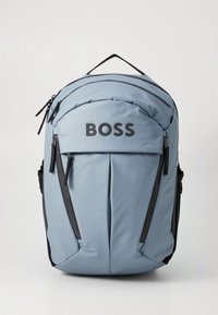 Vaaleansininen reppu mustilla yksityiskohdilla, vetoketjullisilla osastoilla ja edessä näkyvästi esillä oleva "BOSS"-logo. Teksturoidu kangas.