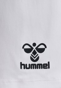 Biały materiał z czarnym logo o zaokrąglonych kształtach i stylizowanym wzorem pszczoły. Nazwa marki "hummel" znajduje się pod logo.